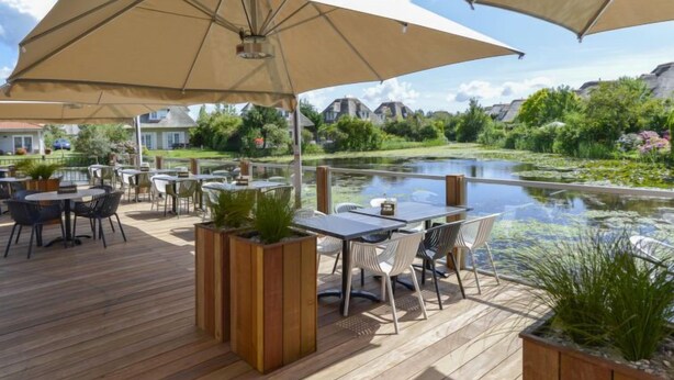 Eine Außenpatio mit Holztischen und -stühlen, großen Sonnenschirmen und Pflanzkübeln.