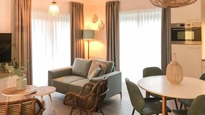Ein modernes Wohnzimmer mit einer Couch, Sesseln, einem Esstisch und einem Fernseher.