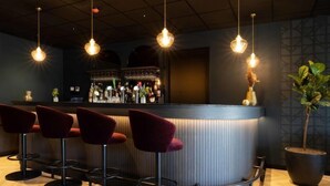 Eine Bar mit einer gebogenen Theke, vier roten Barhocker, hängenden Pendelleuchten und einem Blumentopf.