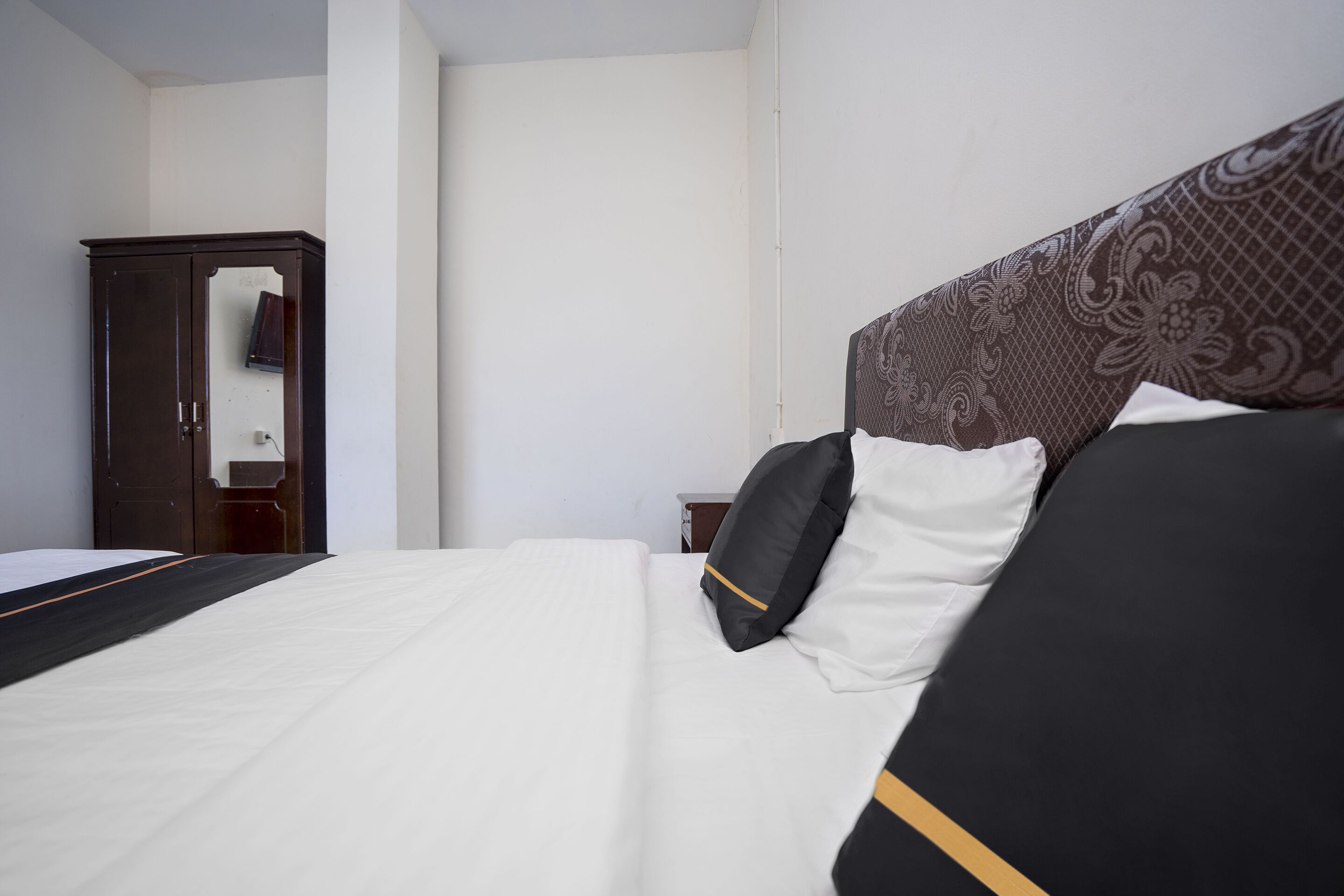 Ein Hotelzimmer mit einem ordentlich bezogenem Bett, einem Holzschrank und einer schlichten weißen Wand.