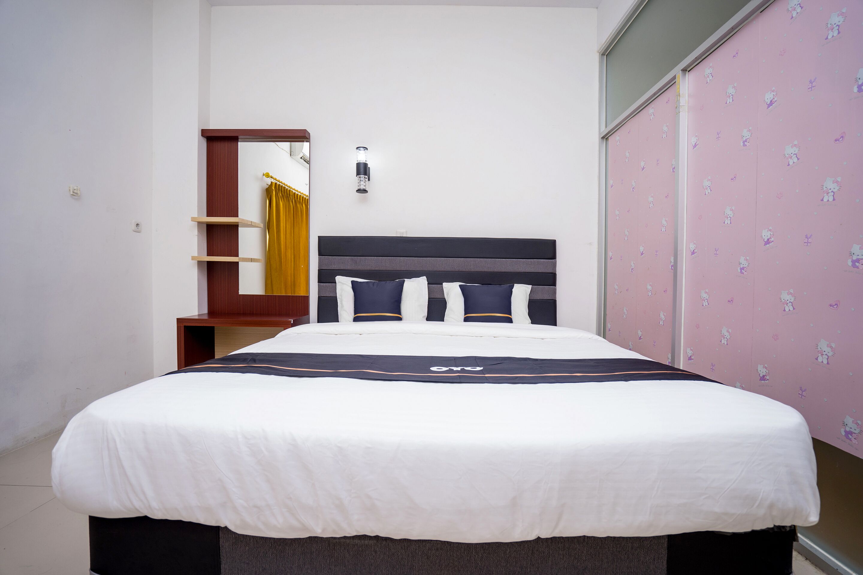 A neatly made bed with a dark headboard, a bedside table, and a wall-mounted light fixture.