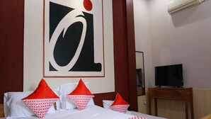 Una habitación de hotel con una cama, almohadas, un televisor y una obra de arte en la pared.