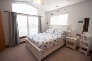 Een slaapkamer met een bed, nachtkastjes, een raam met gordijnen, een plafondventilator en wanddecoraties.