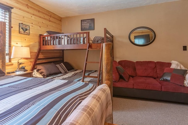 Una cama litera con escalera, un sofá rojo y un espejo instalado en la pared.