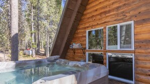 Una cabaña de madera con jacuzzi, ventanas amplias y vistas al bosque circundante.