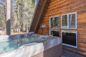 Una cabaña de madera con un jacuzzi y ventana con vistas a un bosque.