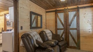 Interior acogedor de una cabaña con un sofá de cuero, un espejo y una puerta corredera de estilo rústico.
