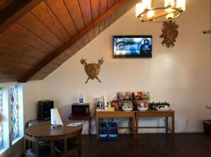 A dining area with a wooden ceiling, a television mounted on the wall, and a table with food and drinks.