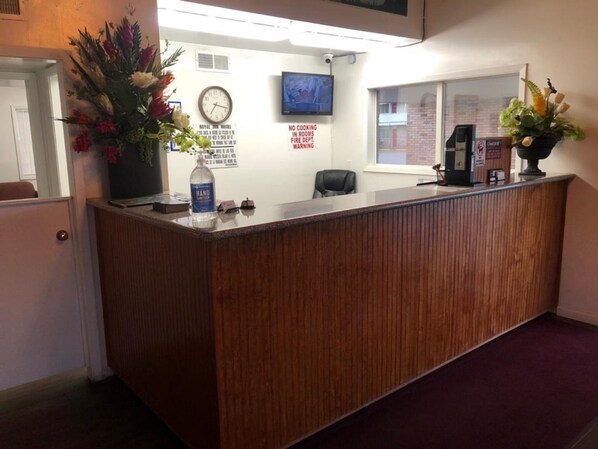 A hotel reception desk with a clock, a TV, and a 'No Cooking in Fire Dept. Warning' sign.
