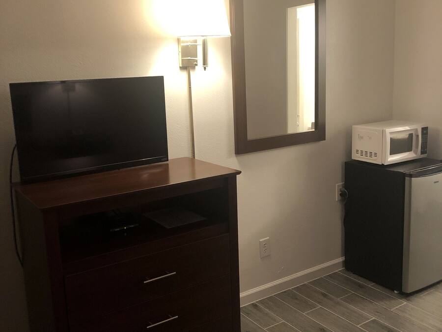 Una habitación con una televisión de pantalla plana sobre un mueble de madera, un microondas y un espejo montado en la pared.