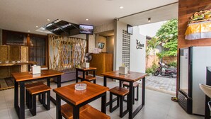 Un restaurante con mesas y bancos de madera, un televisor montado en la pared y vista a la calle.