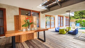 Una terraza de madera con una zona de bar, asientos al aire libre y una piscina al fondo.