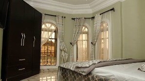 A bedroom with a large bed, dark wardrobe, and arched windows with curtains. - Exquisite home. Perfect home away from home (Lagos Mainland)