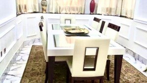 A dining area with a marble floor, white table with dark chairs, and beige curtains. - Exquisite home. Perfect home away from home (Lagos Mainland)