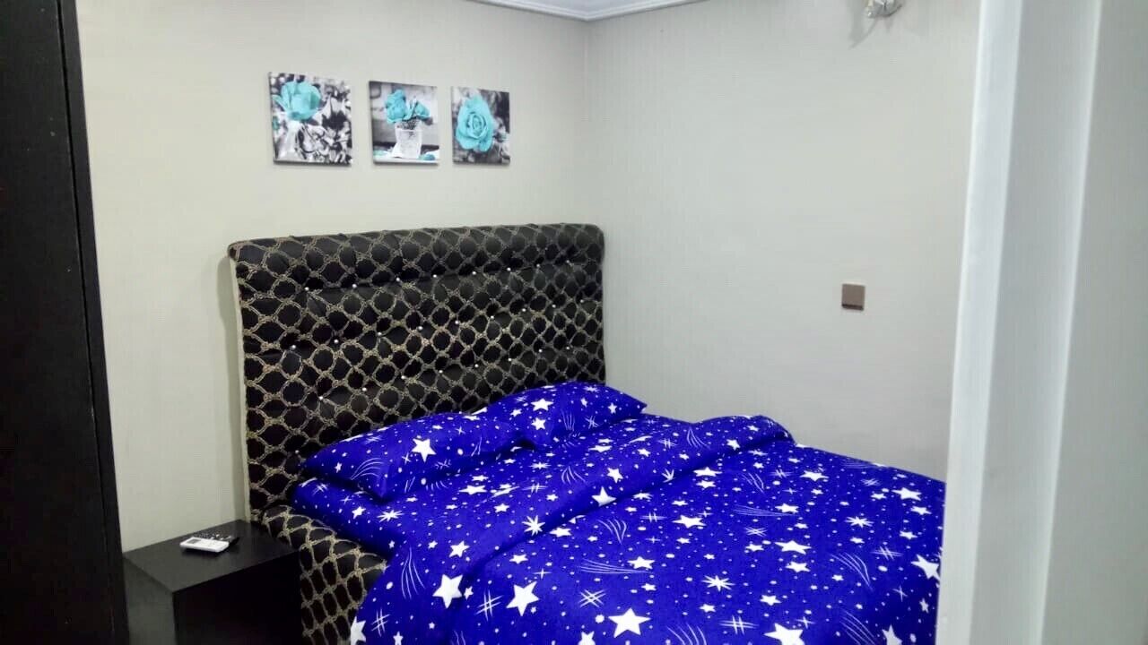 A bedroom with a patterned headboard, a blue bedspread with white stars, and a nightstand with a remote control.