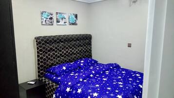 A bedroom with a patterned headboard, a blue bedspread with white stars, and a nightstand with a remote control.