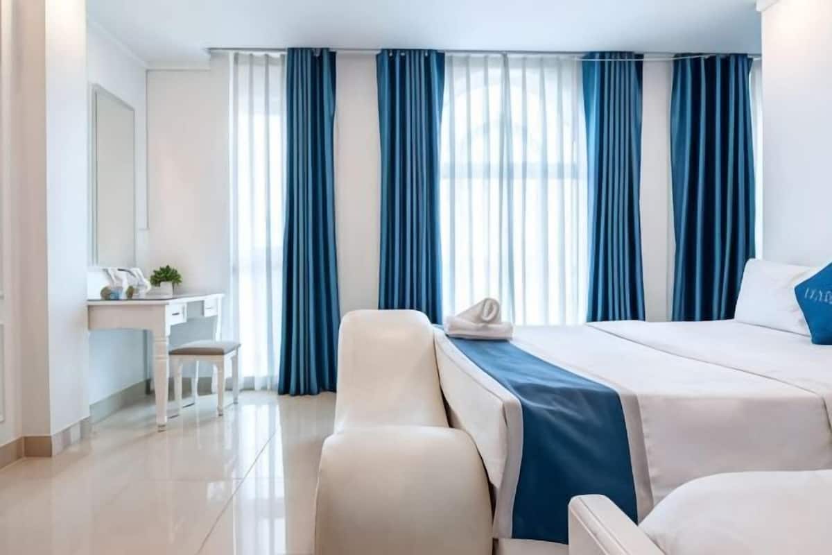 Habitación de hotel con cama, escritorio, silla y un amplio ventanal con cortinas.