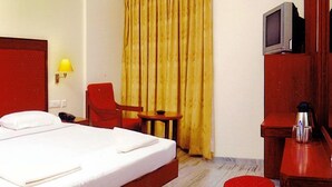 A hotel room with a bed, a chair, a small table, a lamp, and a television. - The Golden Park (Madurai)