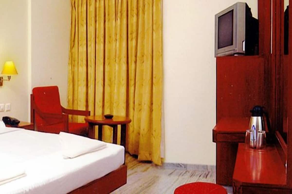 Habitación de hotel con cama, una silla, una mesita, lámpara y televisor.