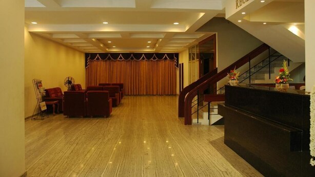 A reception area with a staircase, a reception desk, and a seating area with chairs and a fan. - The Golden Park (Madurai)