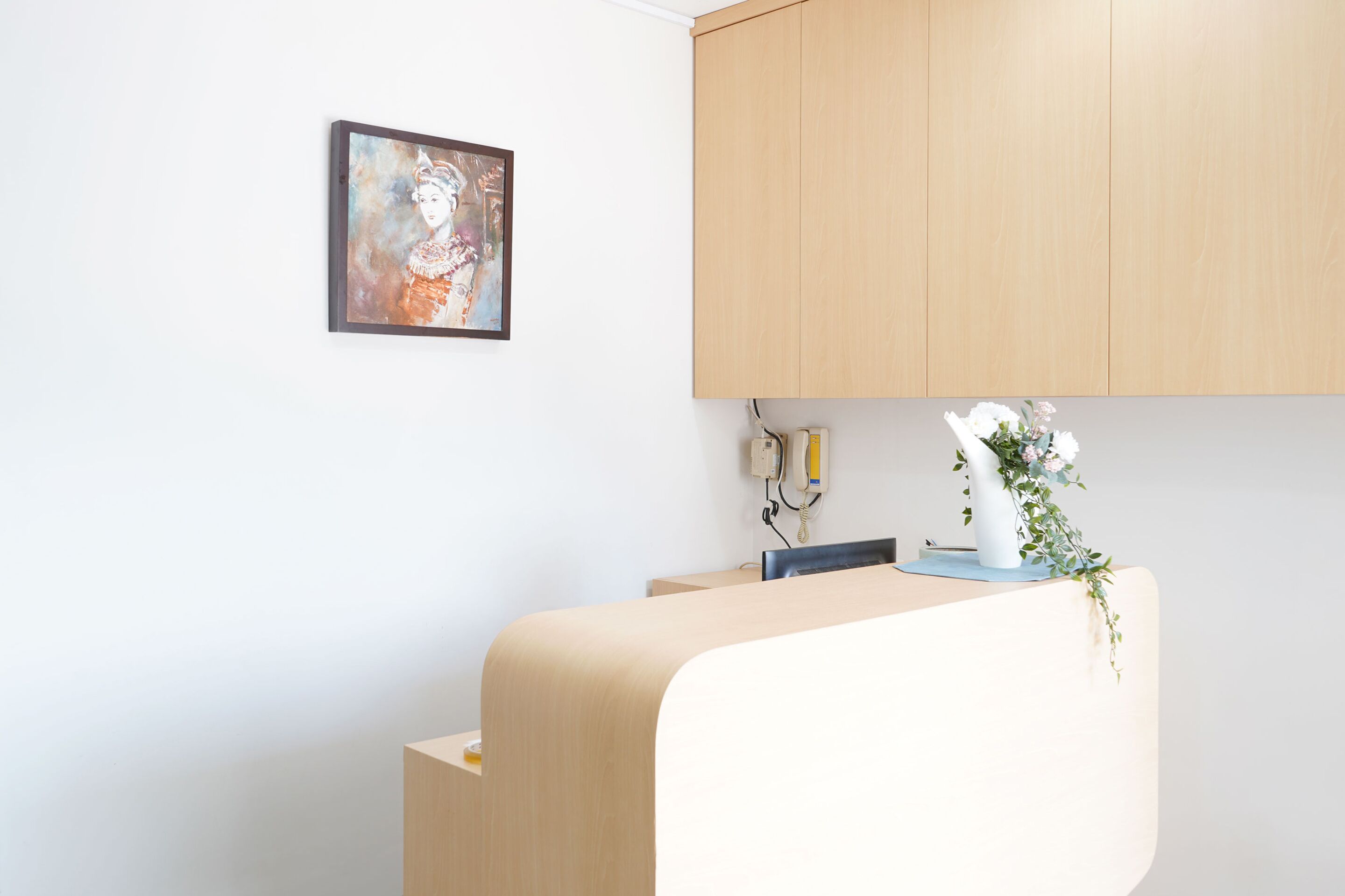 A modern reception area with a wooden cabinet, a framed artwork on the wall, and a vase with flowers on the counter.