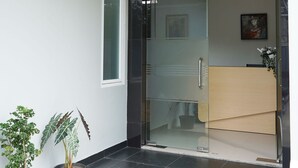Una entrada moderna amb una porta de vidre, plantes en testos i un paviment de rajoles.