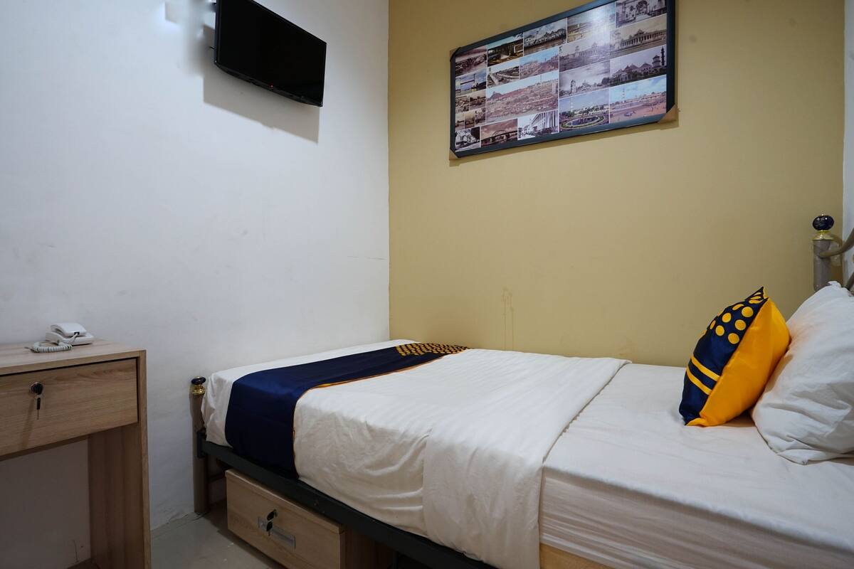 A bedroom with a bed, a bedside table with a phone, a wall-mounted TV, and a framed collage of photos on the wall.
