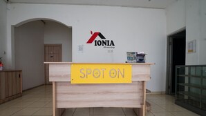 A reception desk with a "SPOT ON" sign, a logo for "IONIA Homestay," and a wooden cabinet to the left.