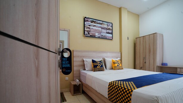 A hotel room with a bed, a wooden wardrobe, a small bedside table, and a wall-mounted photo collage.