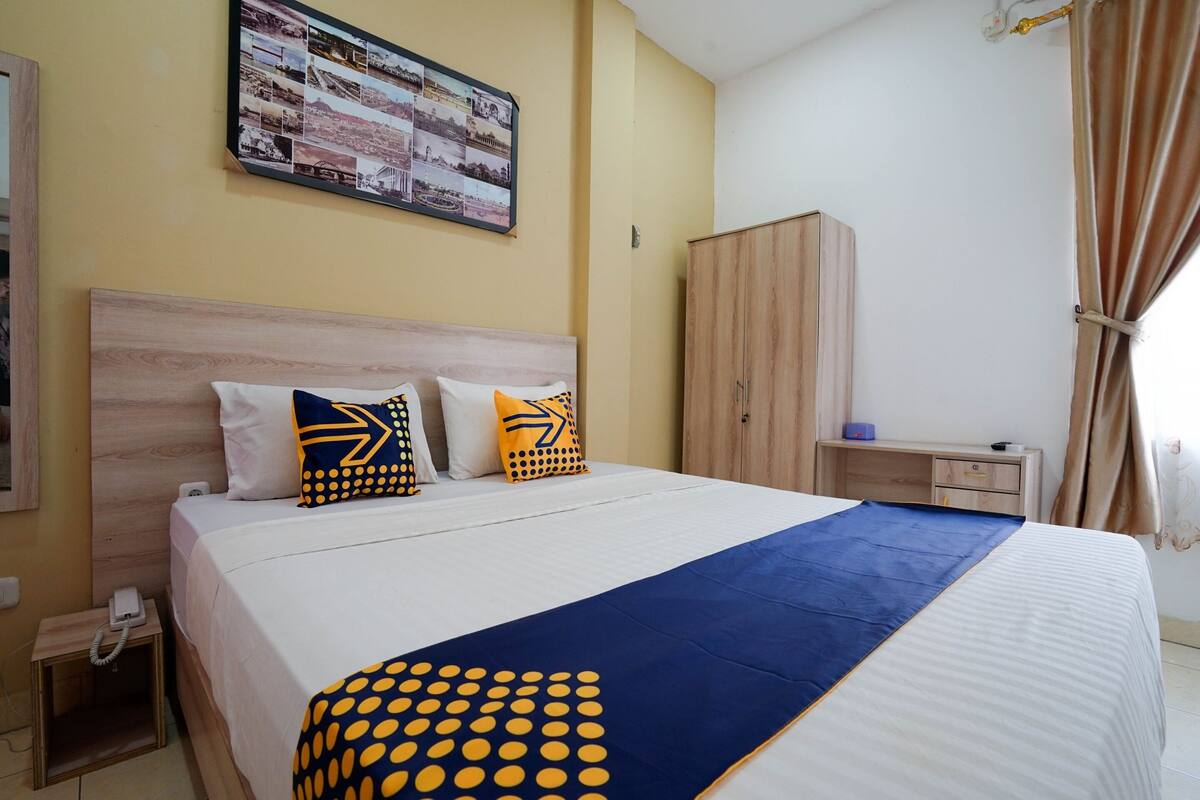 A hotel room with a large bed, a wooden wardrobe, a bedside table, and a wall-mounted photo collage.