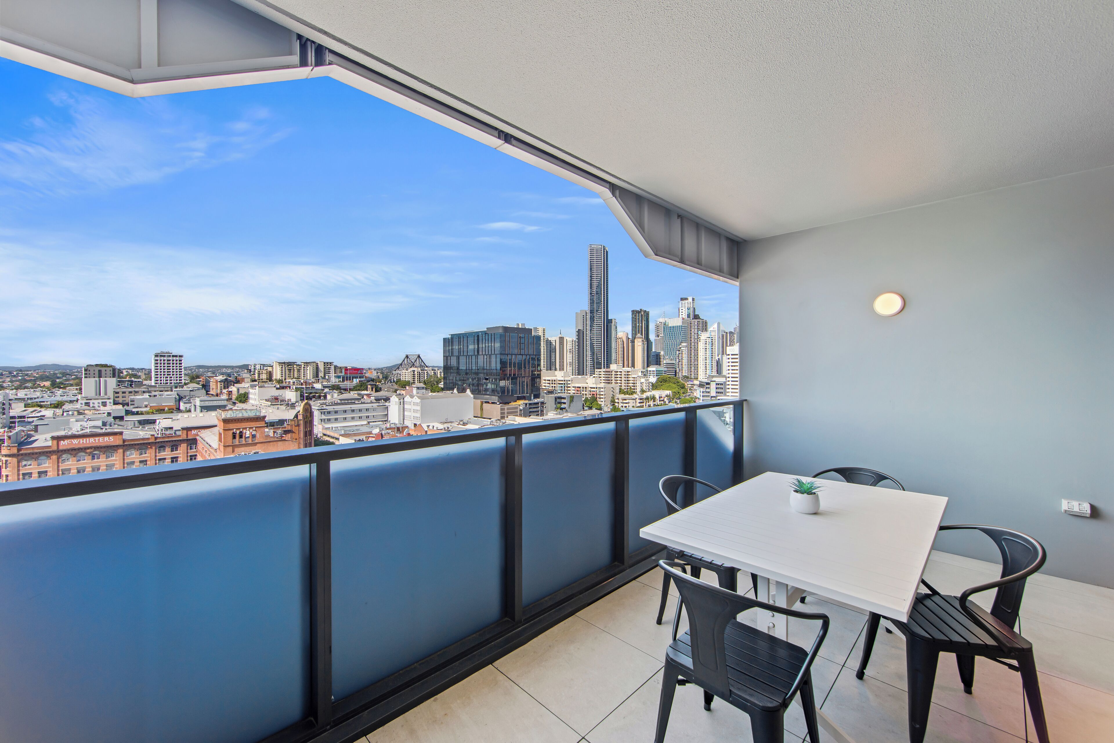 A balcony with a city view, a white table, and black chairs.