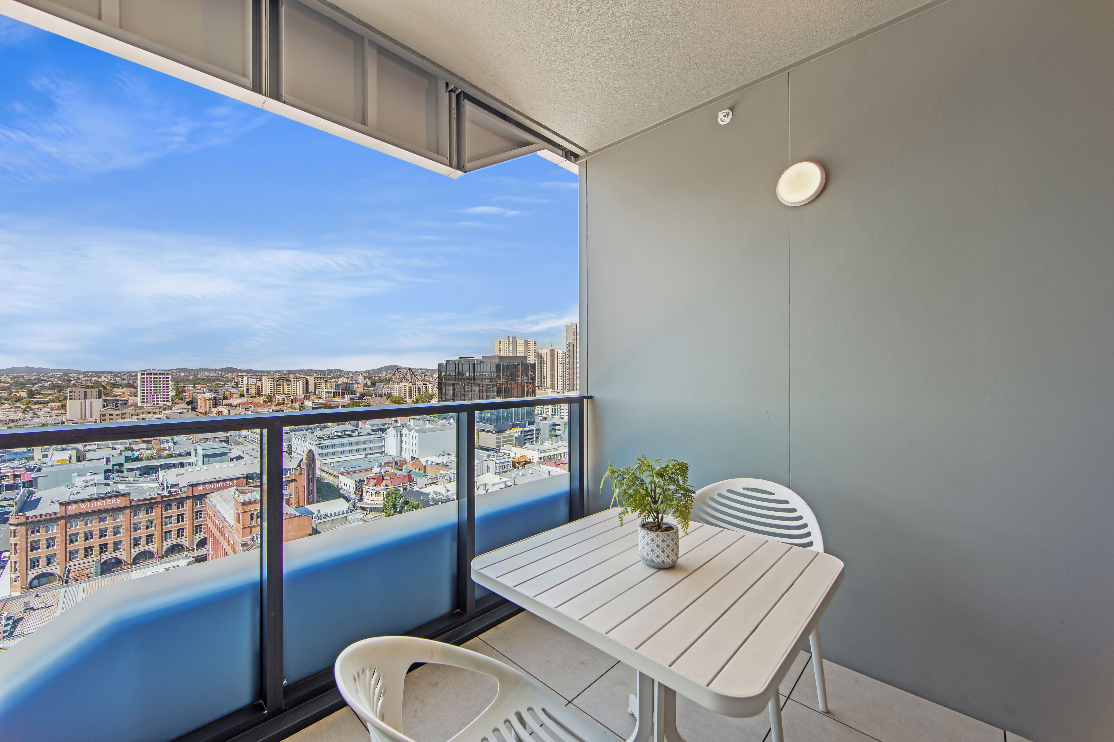 A balcony with a table and chairs, a potted plant, and a city view.