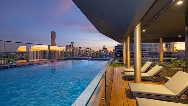 Una piscina en la azotea con sillas de descanso, vista al horizonte de la ciudad y una terraza de madera.
