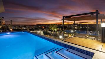 Una piscina con escalones de acceso, rodeada de sillas de descanso y una terraza de madera.