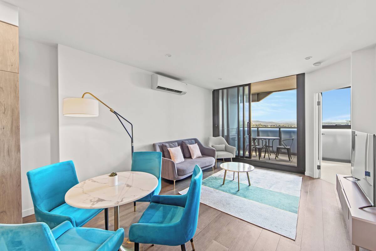 Een moderne woonkamer met een bank, twee blauwe stoelen, een ronde tafel en een televisie.