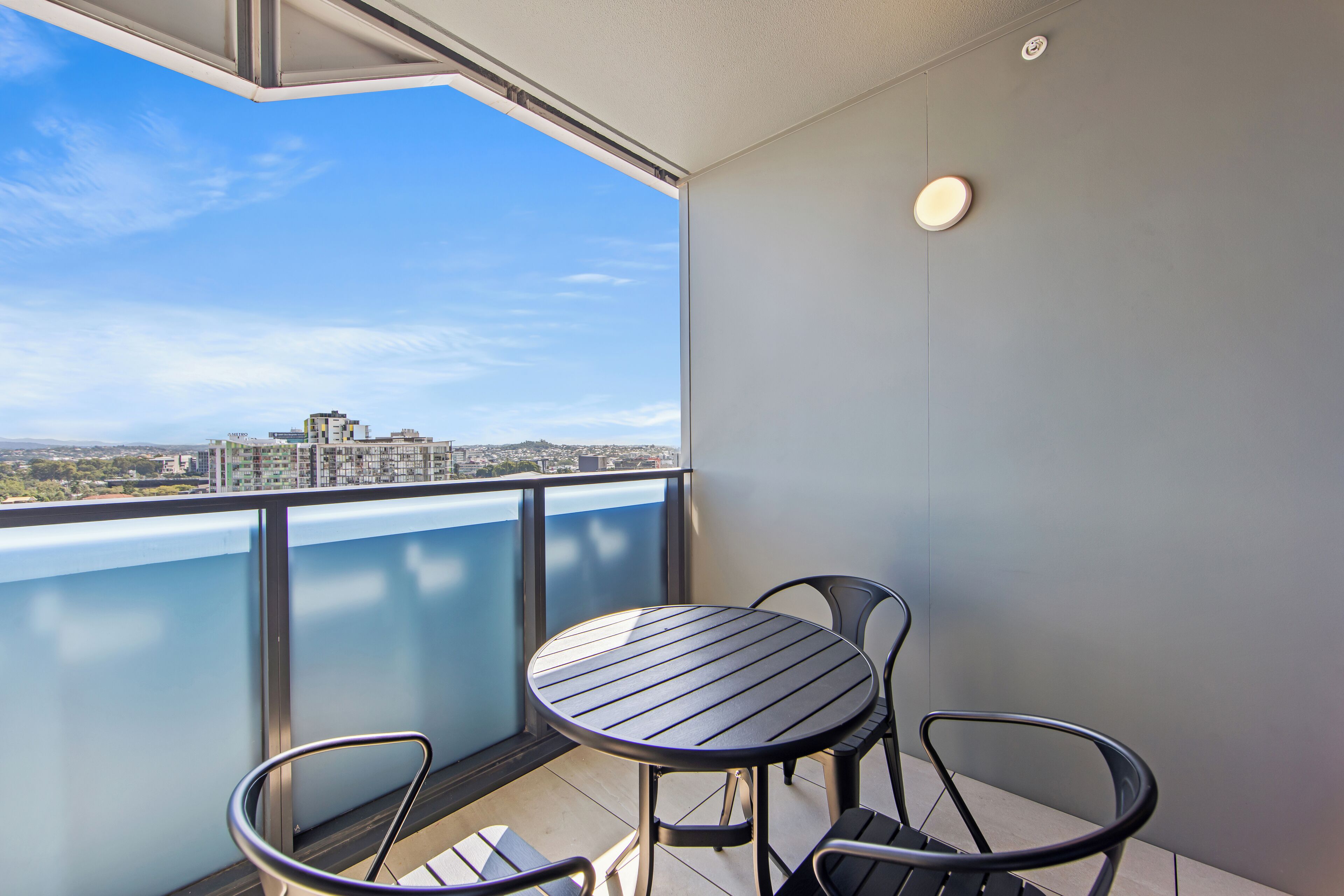A balcony with a table and chairs, a view of the cityscape, and a modern building in the background.