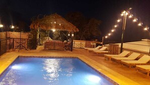 A swimming pool with lounge chairs and a bar area under string lights. - Theodos Lodge Hotel By Hansa (Batroun)