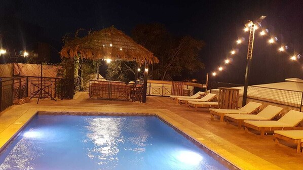 A swimming pool with lounge chairs and a bar area under string lights. - Theodos Lodge Hotel By Hansa (Batroun)