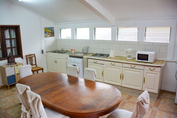A kitchen with a wooden dining table, white cabinets, a microwave, and a window with blinds.