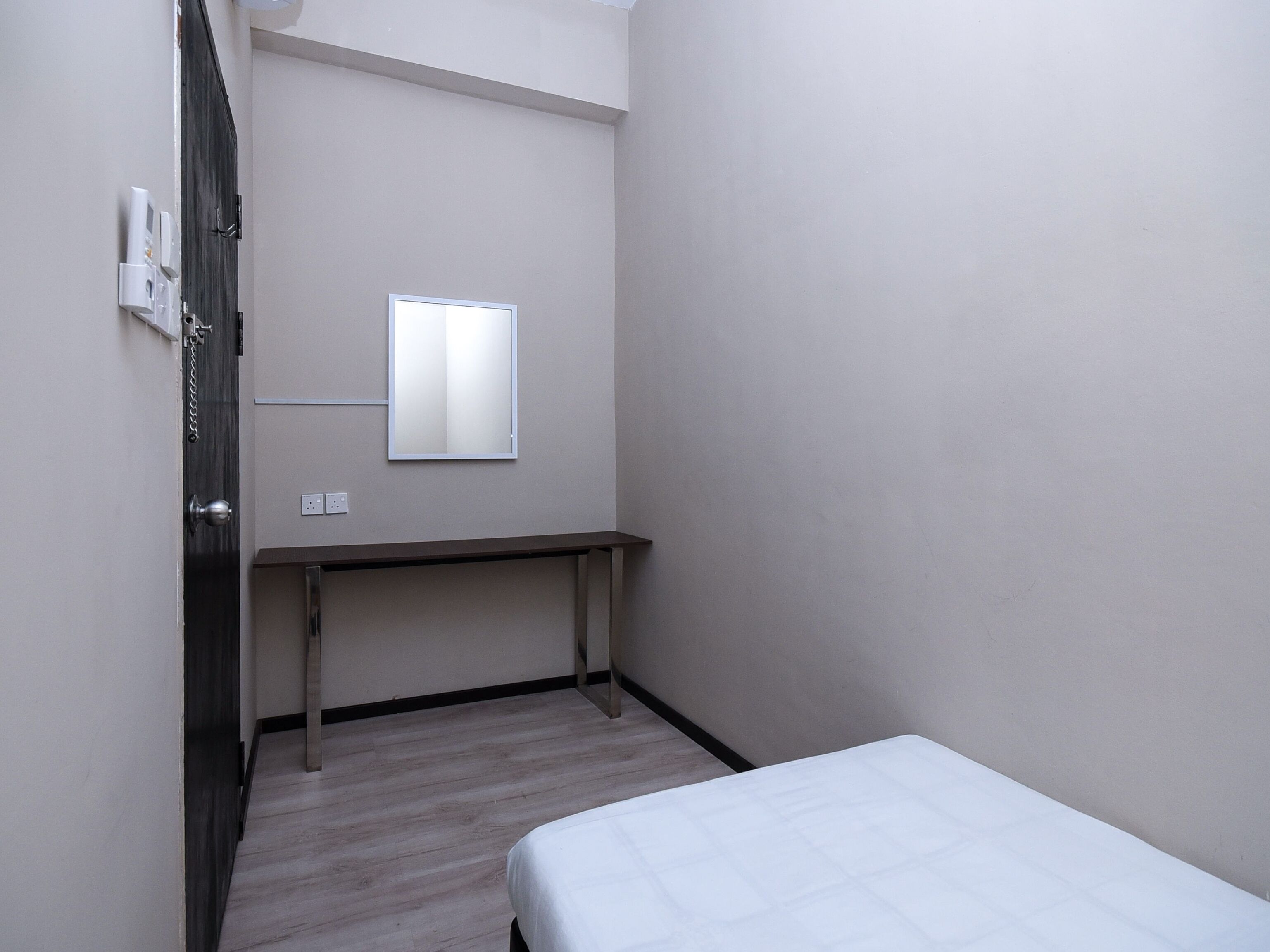 A small, sparsely furnished room with a bed, a desk, and a mirror on the wall.