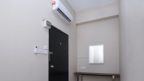Habitación de hotel con una puerta negra, un equipo de aire acondicionado, una mesita de noche y un espejo pequeño en la pared.