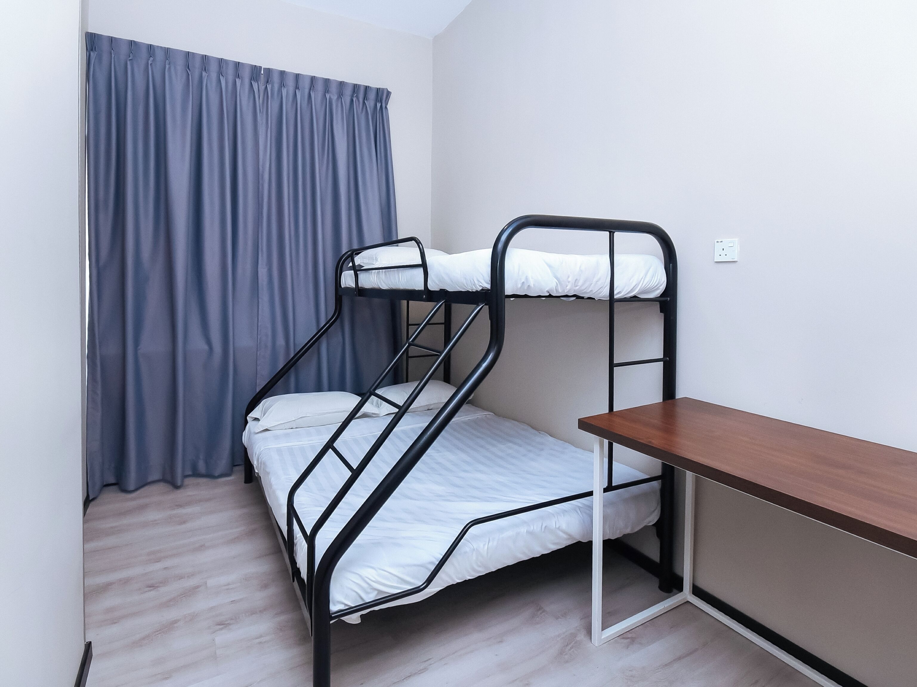 A bunk bed with a wooden desk, a grey curtain, and a light-colored floor.