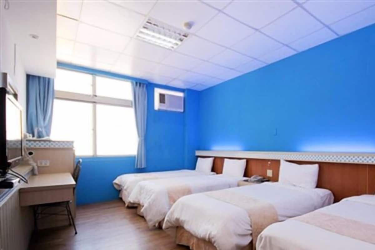 A hotel room with three beds, a desk, and a window with curtains.