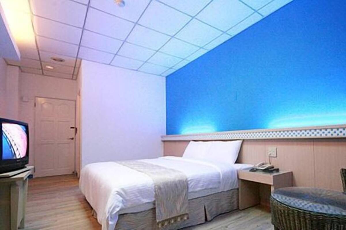 A hotel room with a bed, a television, a chair, and a large window with a view of the sky.