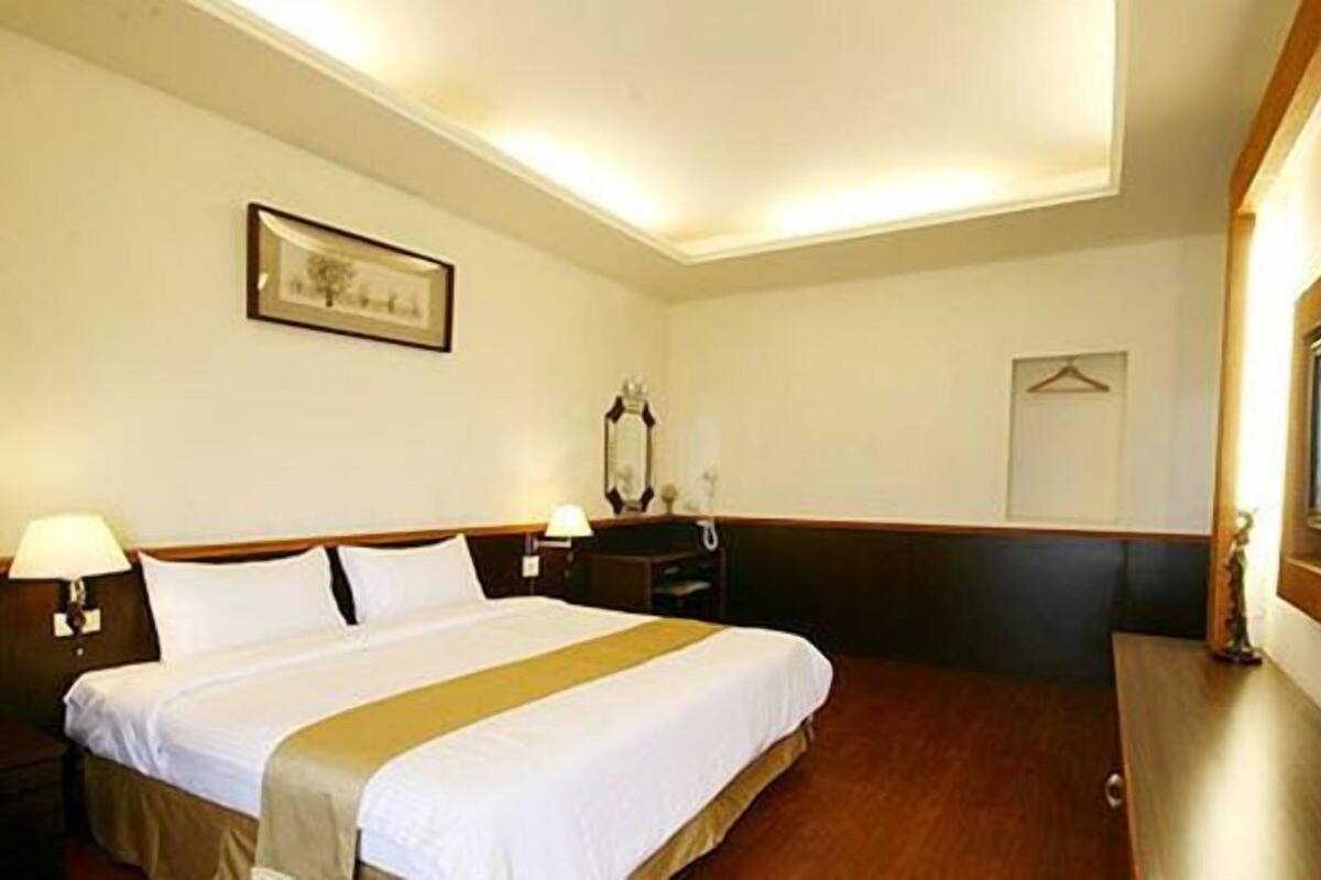 A hotel room with a large bed, two bedside tables with lamps, a mirror, and a framed picture on the wall.