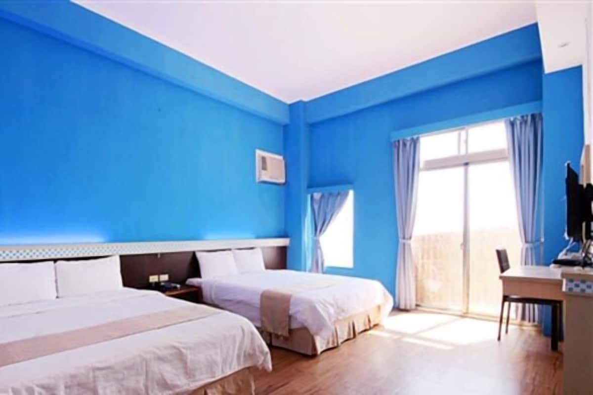 A hotel room with two beds, a desk, and a window with curtains.