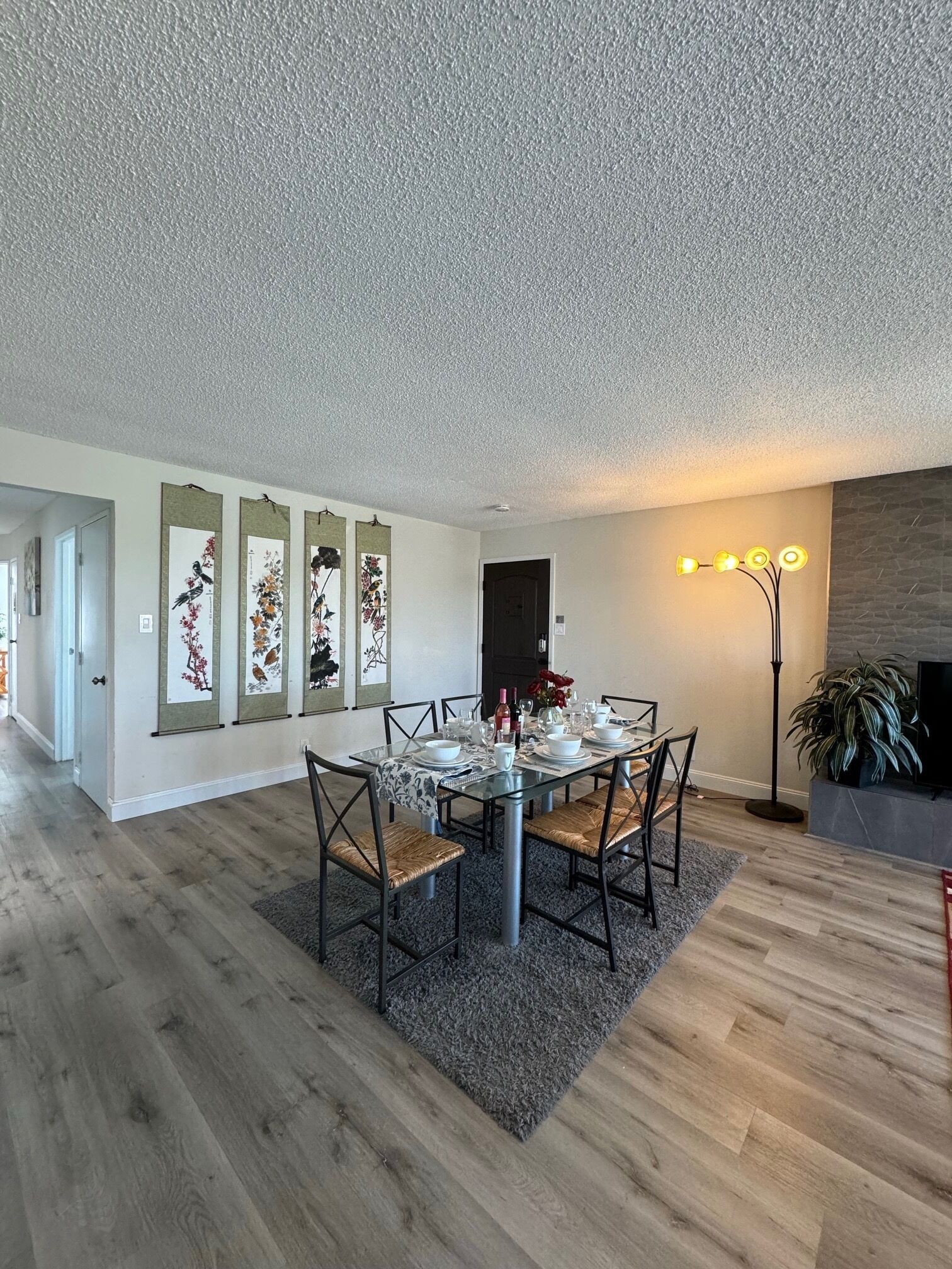 Un coin repas avec une table en verre, des chaises et un tapis. On y trouve des décorations murales et un lampadaire.