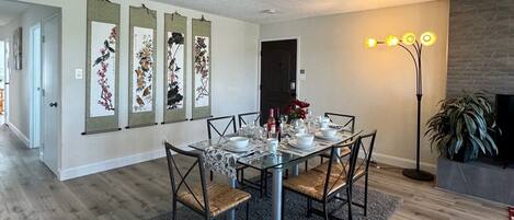 Un coin repas avec une table en verre, des chaises et un tapis. On y trouve des décorations murales et un lampadaire.