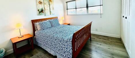 Un dormitorio con una cama de madera, una mesita de noche, una lámpara y una ventana con persianas.