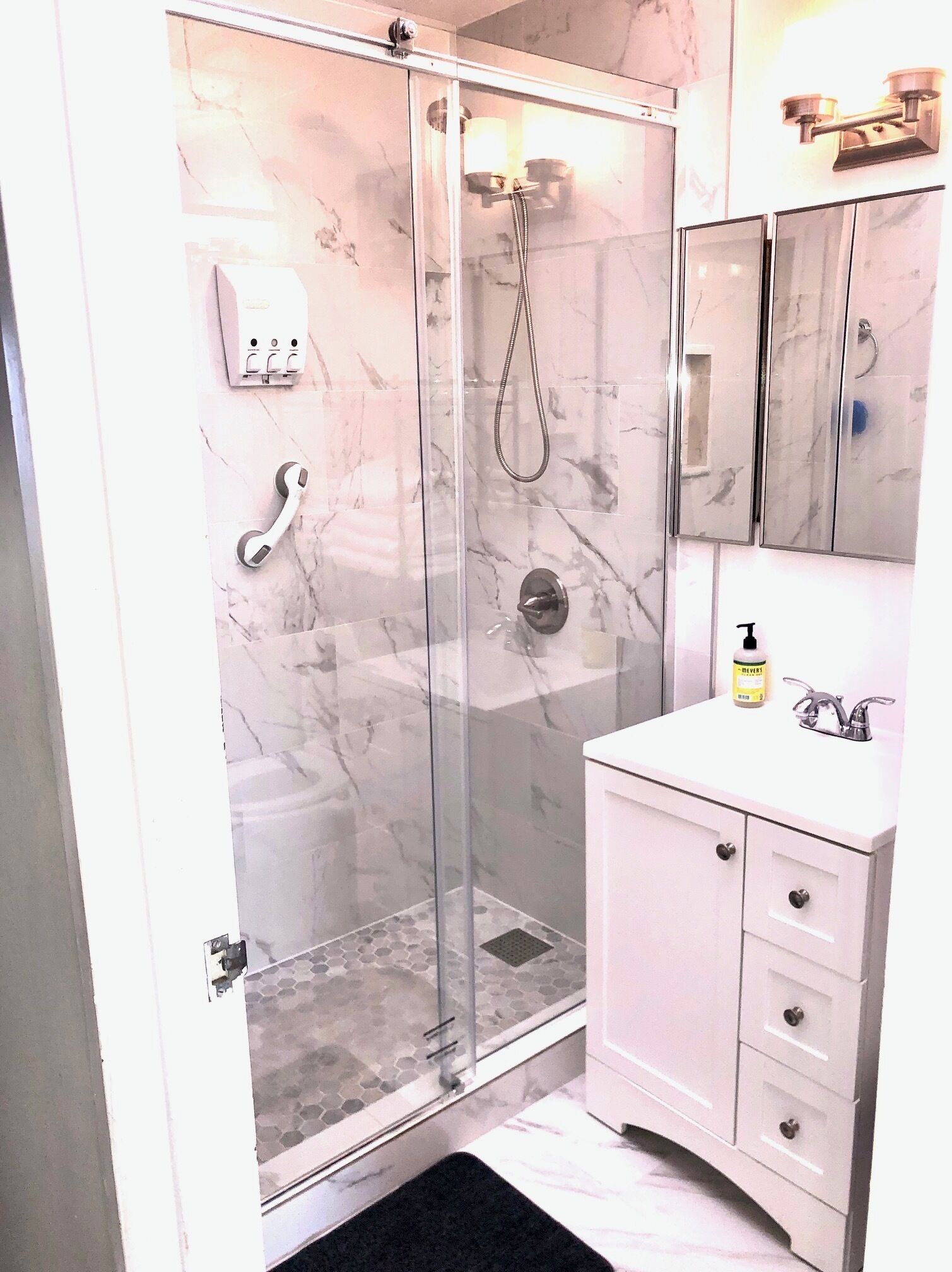 A bathroom with a glass-enclosed shower, a white vanity with a mirror, and a soap dispenser on the counter.